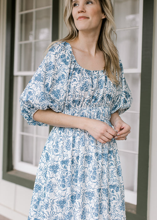 Model wearing a cream midi with blue floral, boat neck, smocked waist and 3/4 bubble sleeves.