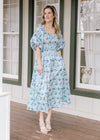 Model wearing heels and a cream midi with blue floral, smocked waist and 3/4 bubble sleeves.