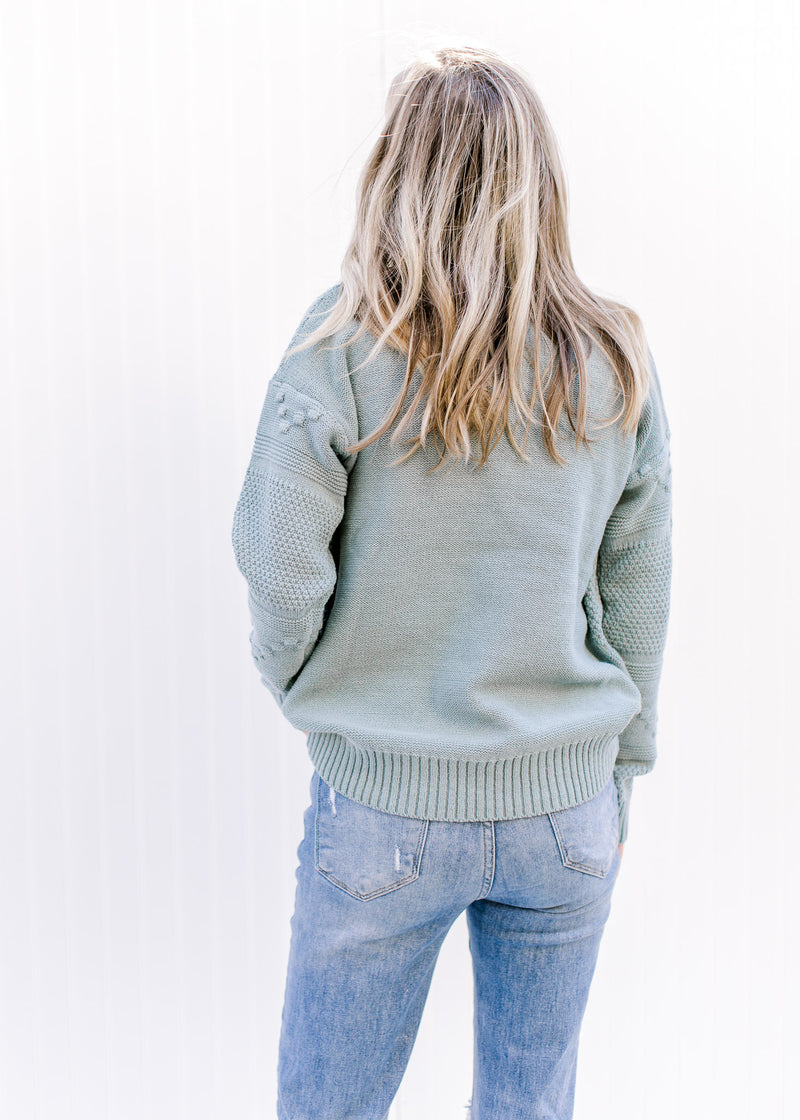 Back view of Model wearing a blue green sweater with a mock neck, long sleeves and ribbed detail.