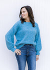 Model wearing an aqua sweater with a boat neck, bubble long sleeves and a rolled hem. 