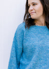 Close up of rolled hem on a boat neck of a aqua blue sweater with long sleeves.