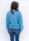 Back view of Model wearing an aqua sweater with a boat neck, bubble long sleeves and a rolled hem. 