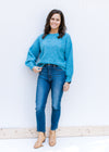 Model wearing jeans and an aqua sweater with a boat neck, bubble long sleeves and a rolled hem. 