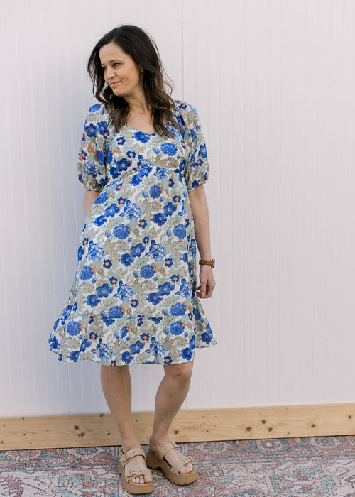 Model wearing a cream babydoll dress with blue, orange and green floral and bubble short sleeves.