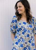 Close up of short puff sleeves and v-neck on a cream dress with green, orange and blue floral. 