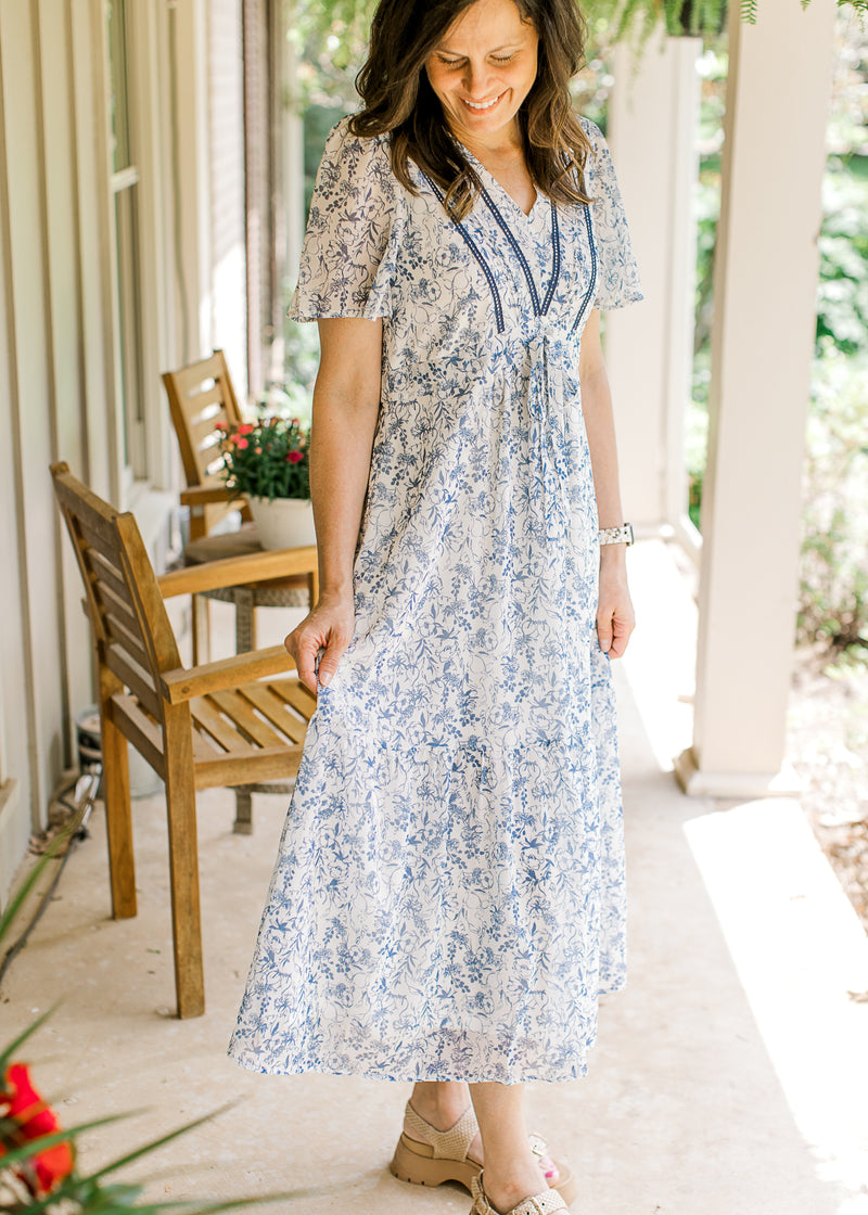 Model wearing a white midi with blue floral, flutter short sleeves, tie waist and a v-neck. 