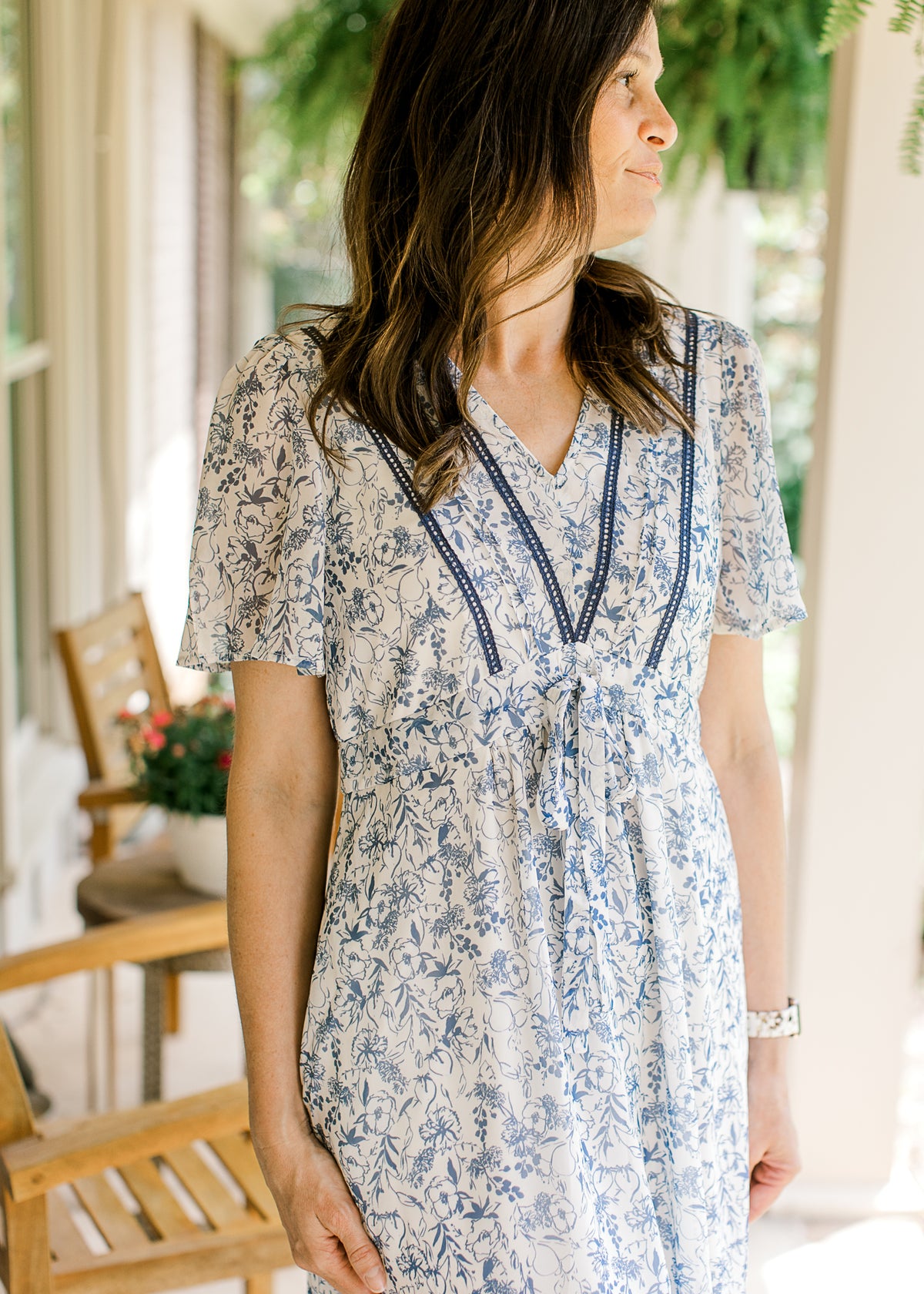 Model wearing a v-neck with double ladder trim and tie at waist of a cream midi with blue floral. 