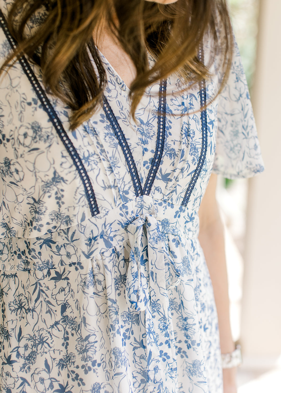 Close up of v-neck with double ladder trim and tie at waist of a cream midi with blue floral. 