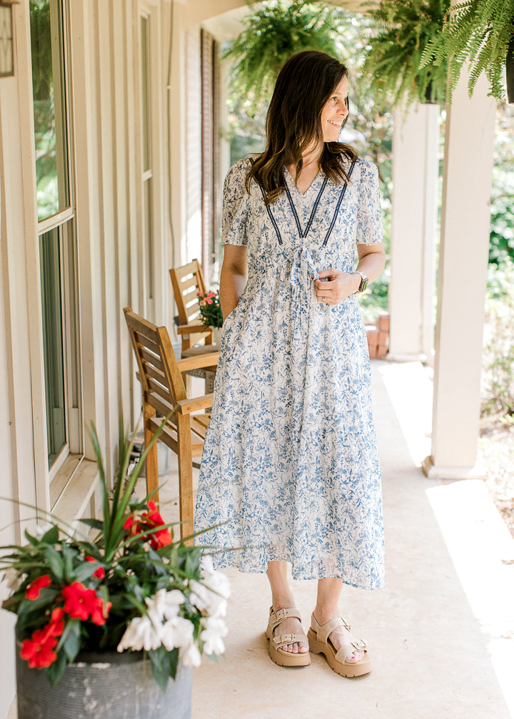 Model wearing wedges and a white midi with blue floral, flutter short sleeves and a v-neck. 