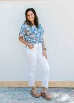 Model wearing white jeans, wedges and a lavender top with flowers, short sleeves and buttons front.