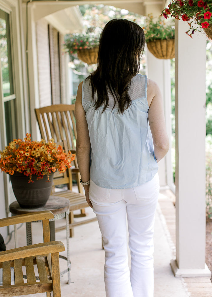 Back view of Model wearing white pants and a sleeveless baby blue top with mesh yoke detail. 