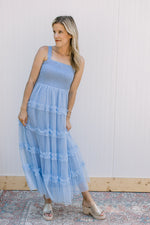 Model wearing a pale blue maxi with a smocked bodice, square neck and a tiered mesh skirt.