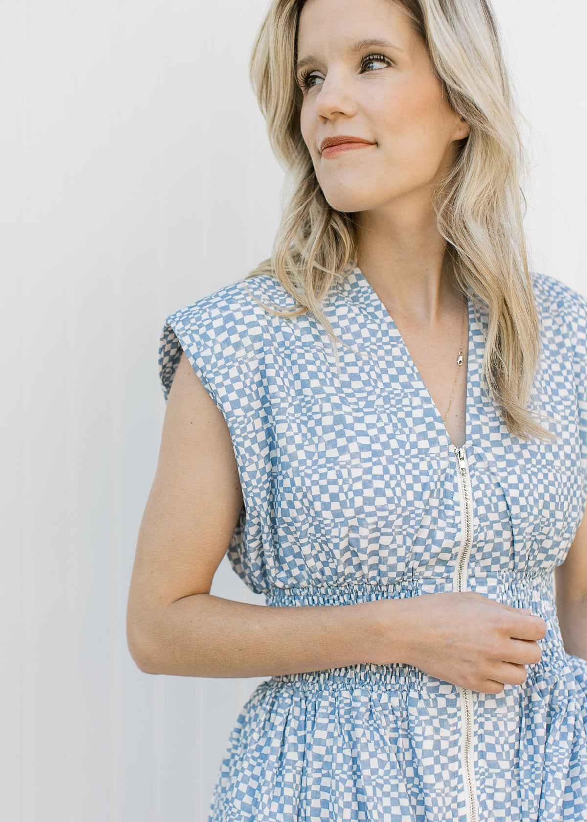 Close up of v-neck, smocked waist and zipper on a blue and white checked sleeveless midi. 