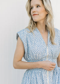 Close up of v-neck, smocked waist and zipper on a blue and white checked sleeveless midi. 