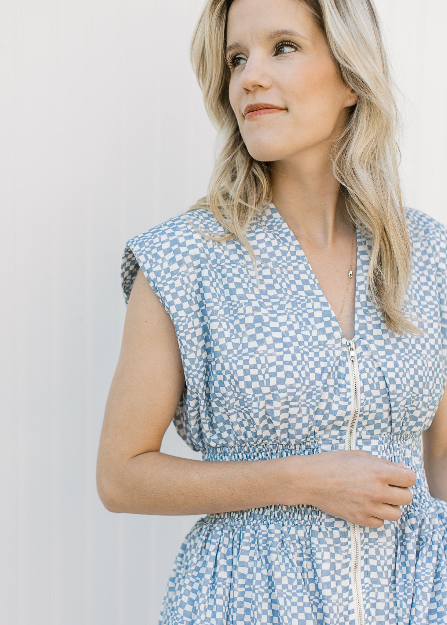 Close up of v-neck, smocked waist and zipper on a blue and white checked sleeveless midi. 