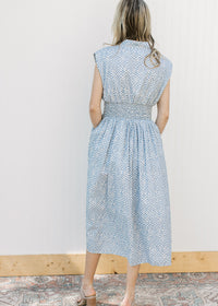 Back view of Model wearing a sleeveless blue and white checked midi with a front zipper. 