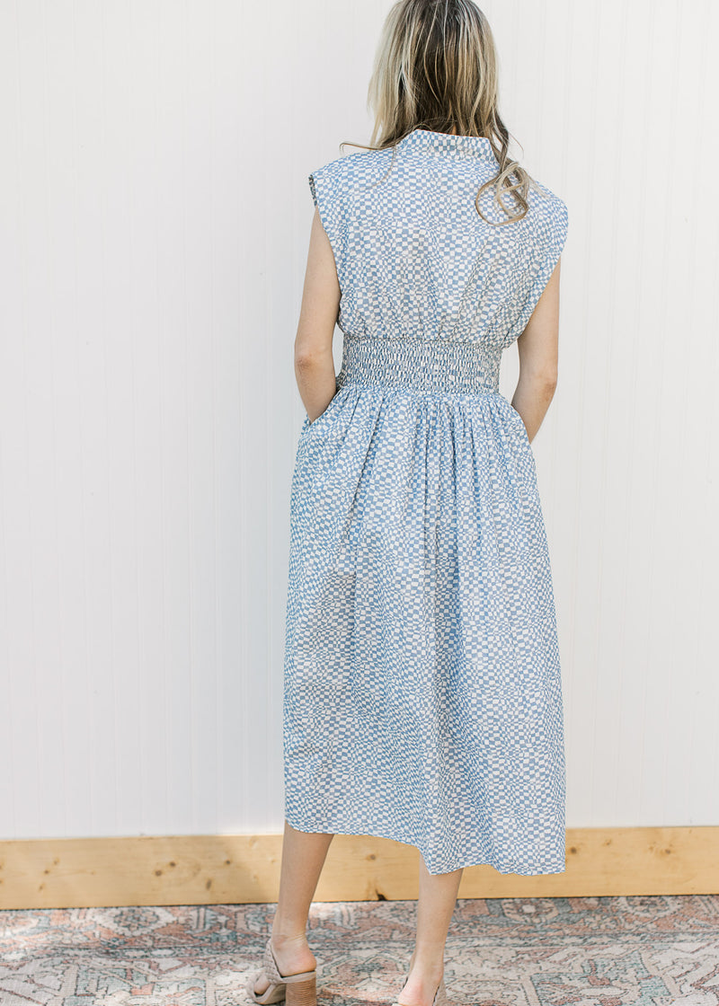 Back view of Model wearing a sleeveless blue and white checked midi with a front zipper. 
