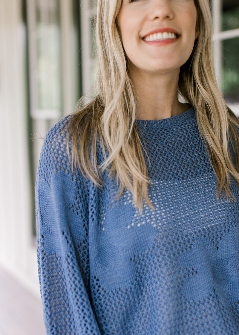 Close up of stitched flowers on a blue open weave sweater with bubble long sleeves. 