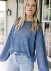 Model wearing jeans and a blue open weave sweater with stitched flowers and bubble long sleeves.