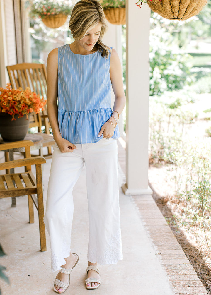 Model wearing white pants, sandals and a blue peplum top with white pinstripes and a round neck.