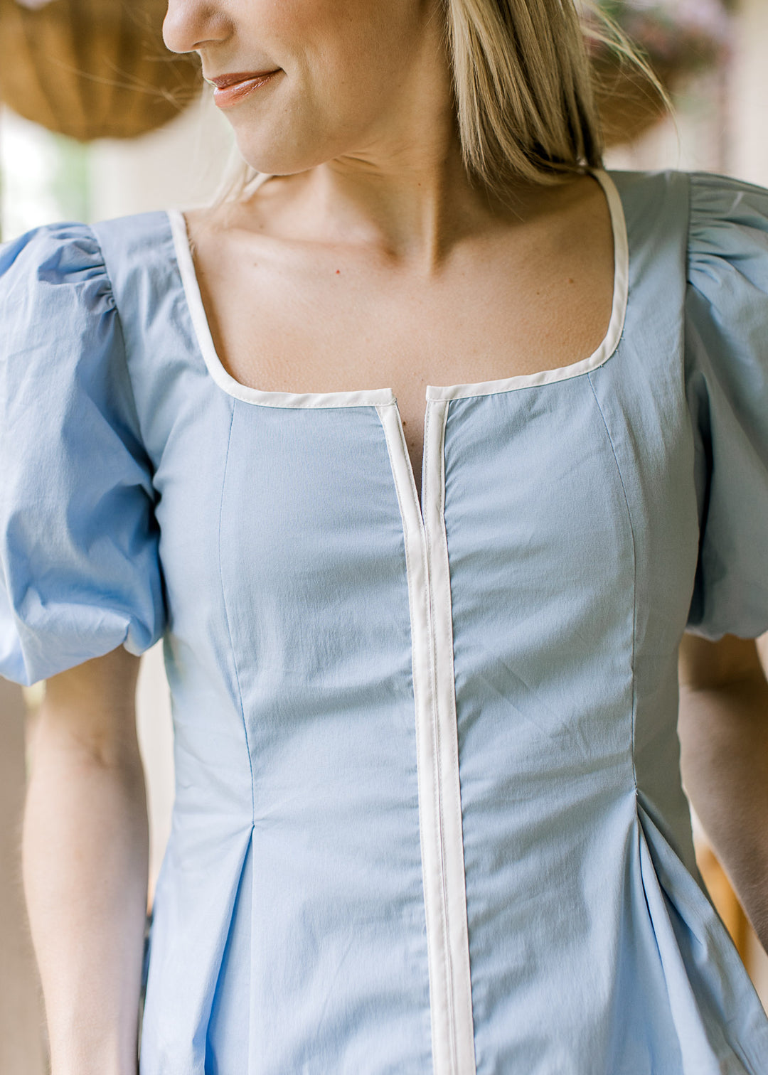 Close up of scoop neck with a v and bubble short sleeves on a baby blu to with white piping.