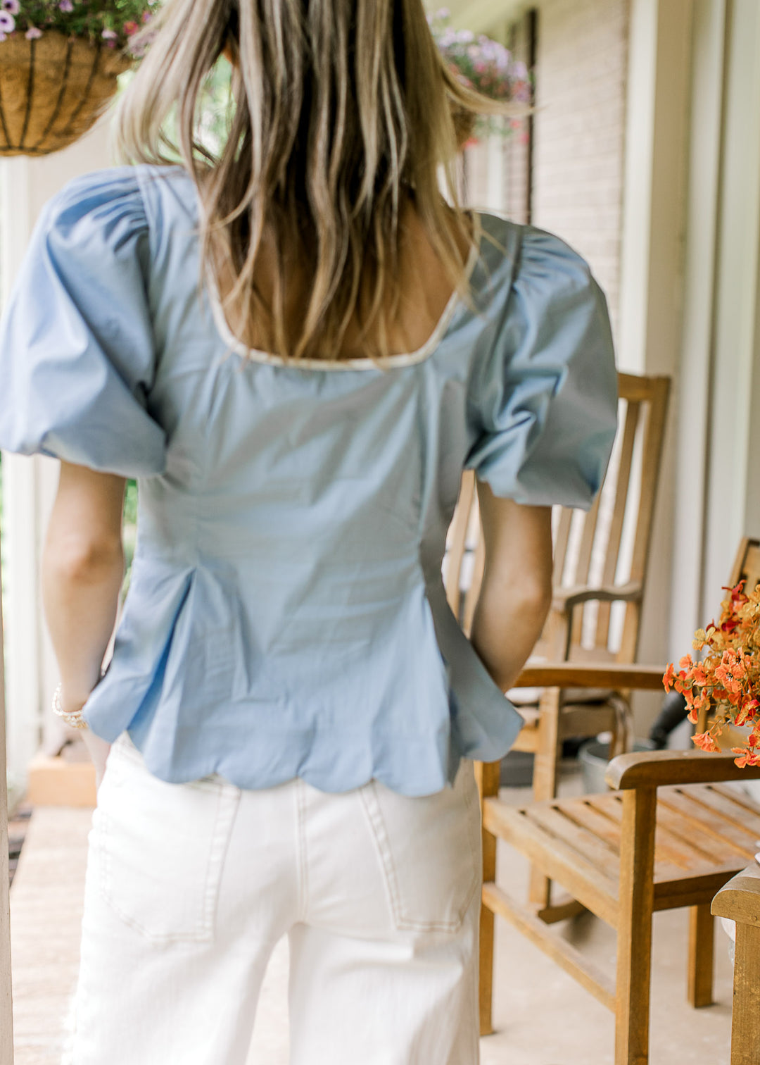 Back view of model in a baby blue top with a scoop neck, scalloped hem an bubble shot sleeves. 