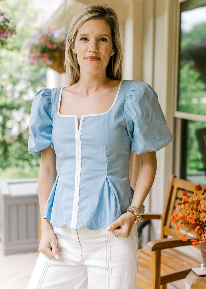 Model wearing a baby blue top with white piping, bubble short sleeves and scalloped hemline. 