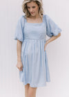 Model wearing a pale blue dress with a pleated bodice, square neckline and bubble short sleeves. 