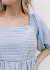 Close up of pleated bodice and square neckline on a pale blue above the knee dress. 