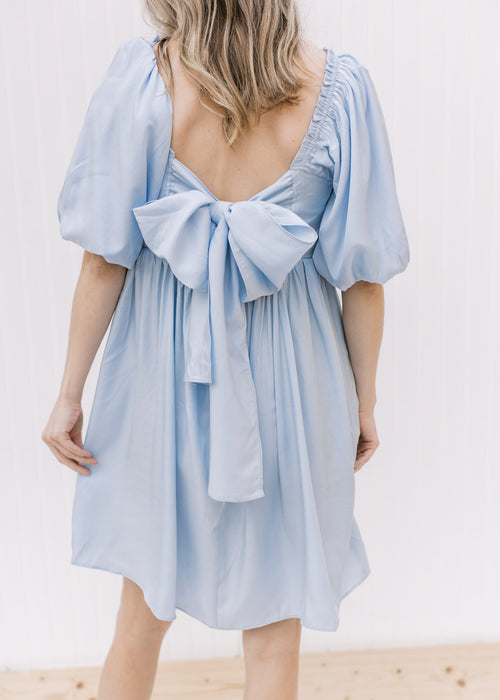 Back view of a pale blue dress with a tie back, bubble short sleeves and a square neck. 