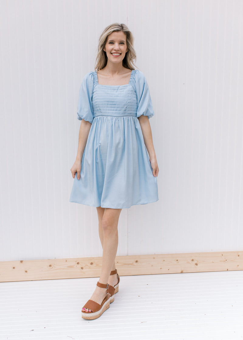 Model wearing heels with a pale blue dress with a square neckline and bubble short sleeves.
