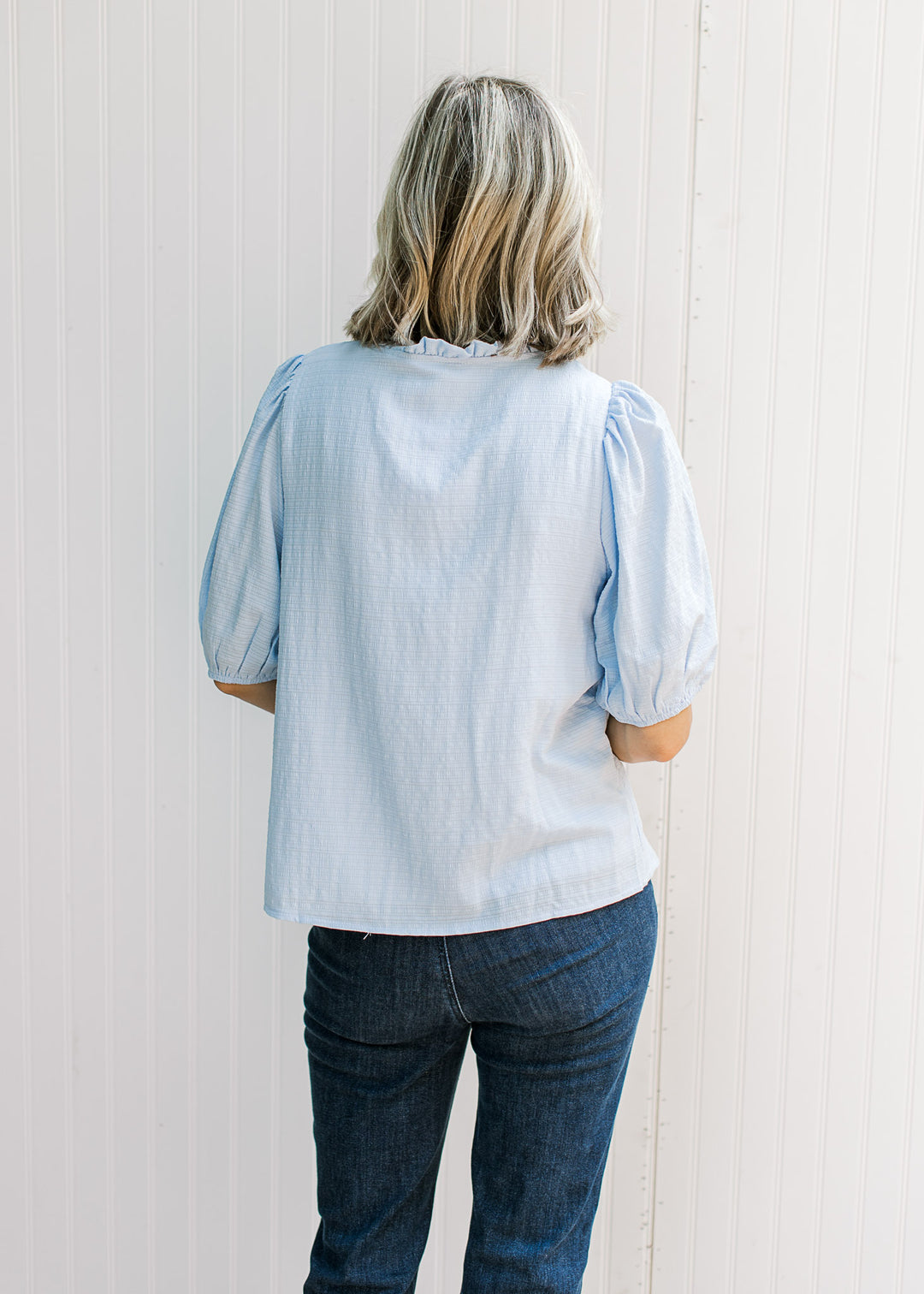 Back view of Model wearing a baby blue top with elbow length sleeves and round neck with ruffle. 