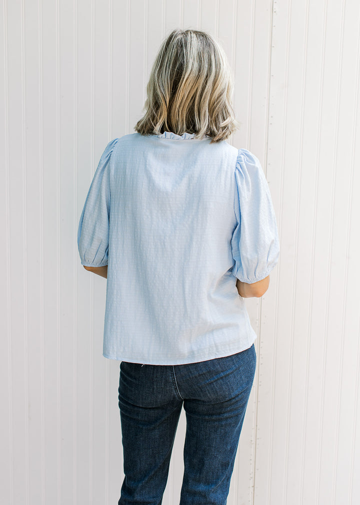 Back view of Model wearing a baby blue top with elbow length sleeves and round neck with ruffle. 