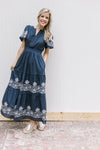 Model wearing a blue dress with a smocked waist short puff sleeves and white stitched flowers.