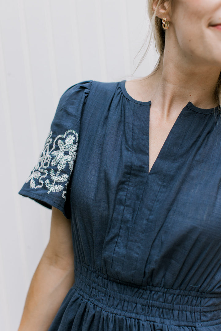 Close up of v-neck and short puff sleeves on a blue maxi with white stitched flowers. 