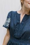 Close up of v-neck and short puff sleeves on a blue maxi with white stitched flowers. 