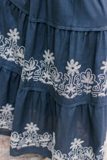 Close up of white stitched flowers on a blue maxi with short sleeves and a v-neck.