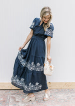 Model wearing a blue maxi with white stitched flowers, v-neck and short sleeves.