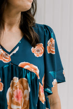 Close up of v-neck and pleated shoulder on a model wearing a navy top with an orange floral pattern.