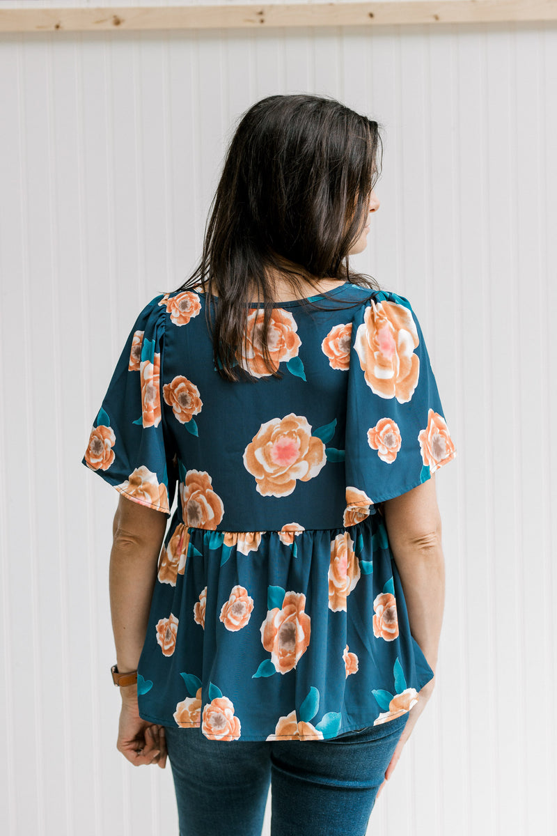Back view of Model wearing a navy babydoll top with an orange floral patter and short sleeves.