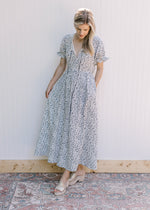 Model wearing a white dress with navy flowers, v-neck with a tie and short sleeves.