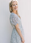 Side view of Model wearing a white dress with navy flowers, v-neck with a tie and short sleeves.