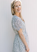 Side view of Model wearing a white dress with navy flowers, v-neck with a tie and short sleeves.