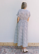 Back view of Model wearing a white dress with navy flowers, v-neck with a tie and short sleeves.