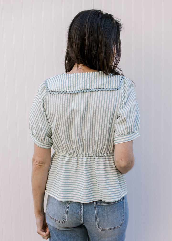 Back view of Model wearing a pale blue and cream striped peplum top with exaggerated collar.