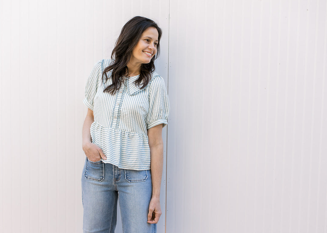 Model wearing a pale blue and cream striped peplum top with a button placket and short sleeves.