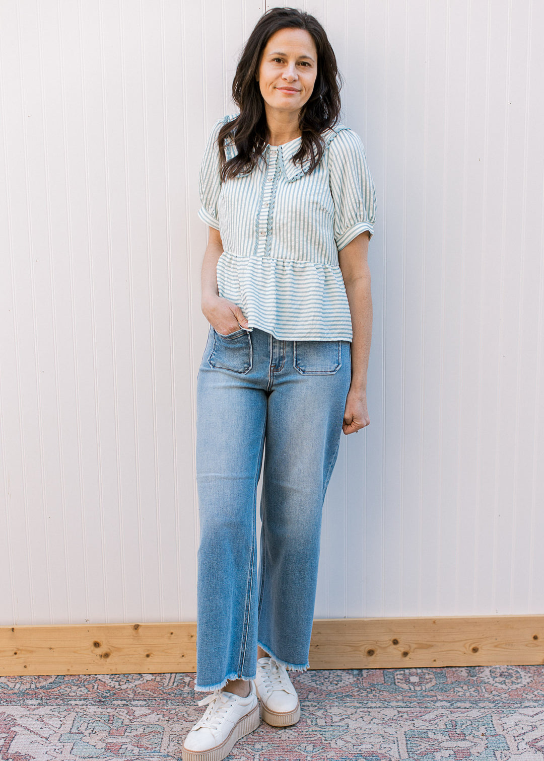Model wearing jeans and a pale blue and cream striped peplum top with short sleeves. 