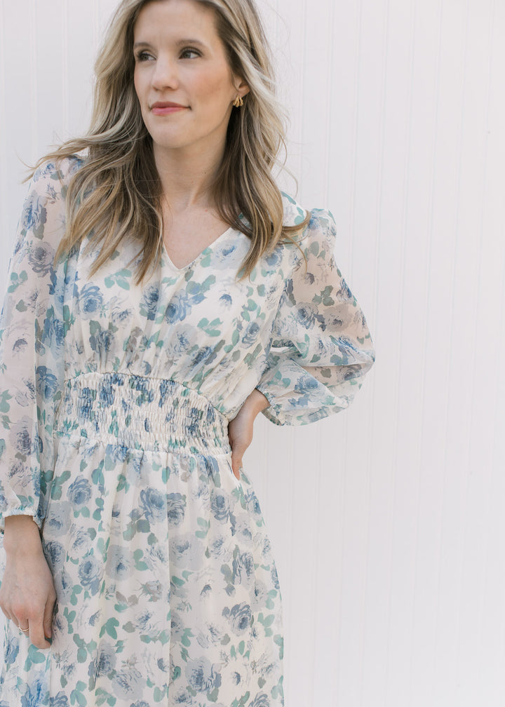 Close up of elastic waist, v-neck and sheer 3/4 sleeves on a cream maxi with blue roses. 