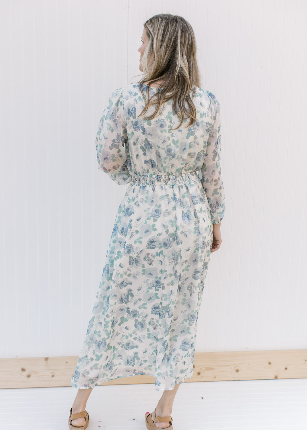 Back view of Model wearing a cream midi with blue roses, an elastic waist and sheer 3/4 sleeves.