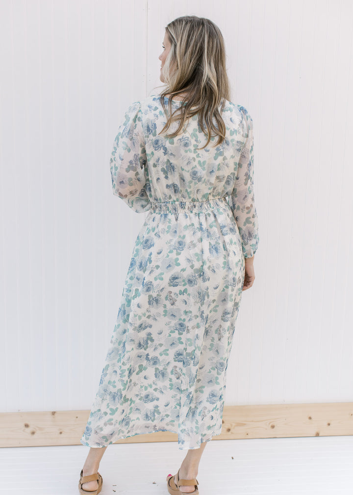 Back view of Model wearing a cream midi with blue roses, an elastic waist and sheer 3/4 sleeves.